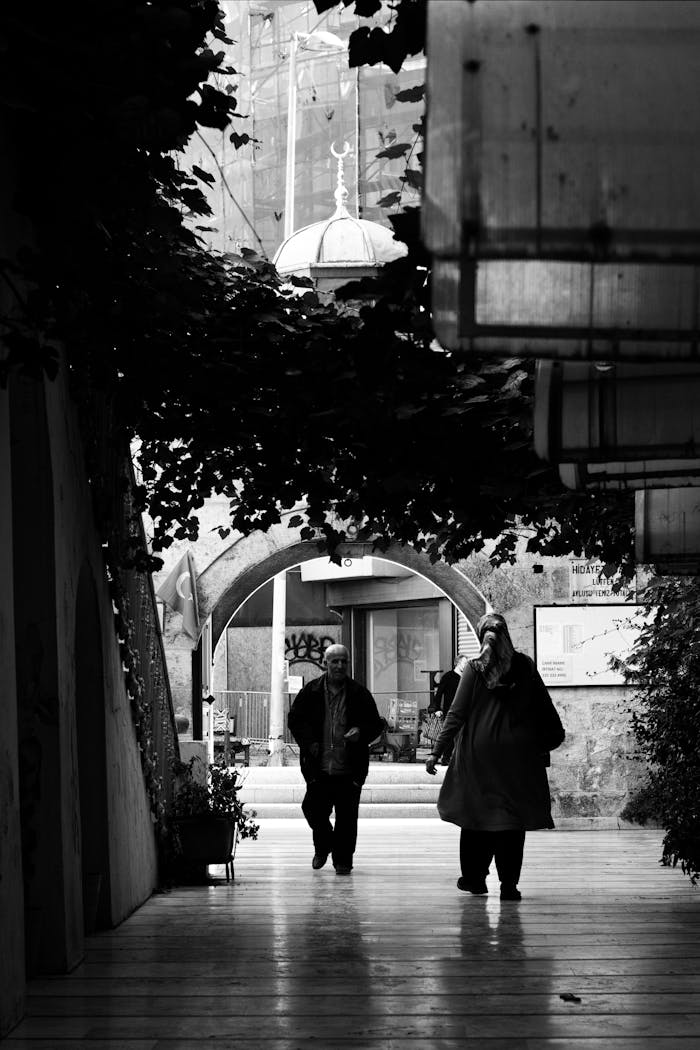 Monochrome image of people walking through an urban alleyway.